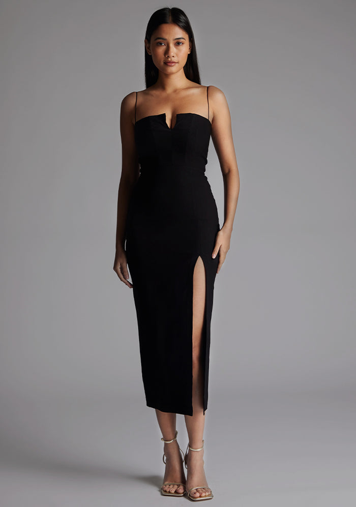 Front image of a model wearing the Vesper Adeline Cut Out Midaxi Dress in Black with a bold V-shaped neckline, slim straps, and sculpting silhouette, standing against a grey studio backdrop.