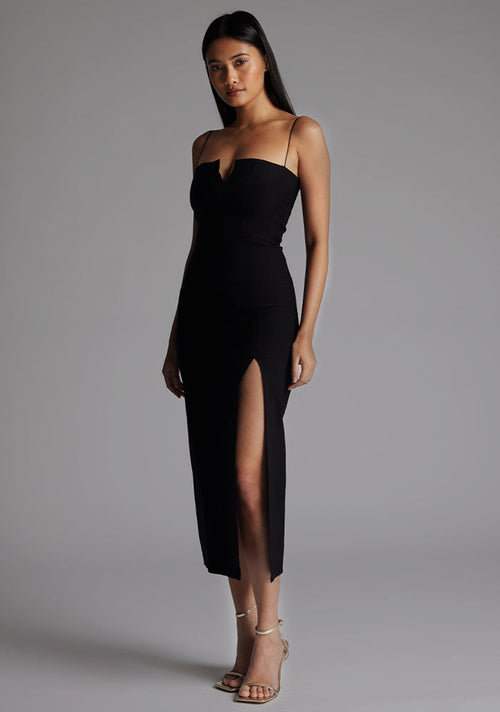 Side front of a model wearing the Vesper Adeline Cut Out Midaxi Dress in Black, emphasizing the sleek midaxi length, front split detail, and figure-enhancing silhouette.