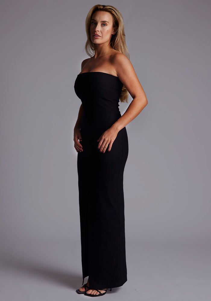 Side front image of a model in the Vesper Alaya Bandeau Maxi Dress in Black, highlighting the smooth strapless silhouette, contoured fit through the waist and hips, and fluid maxi-length drape.