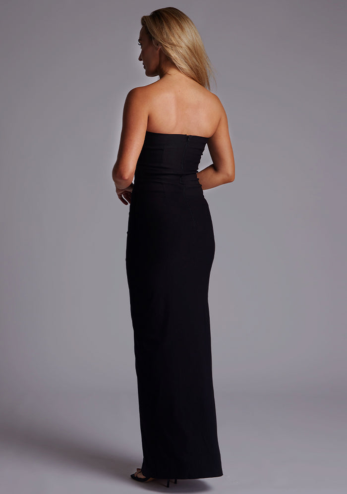 Side back image of a model wearing the Vesper Alaya Bandeau Maxi Dress in Black, revealing the smooth strapless back, tailored fit, and centre-back zip.