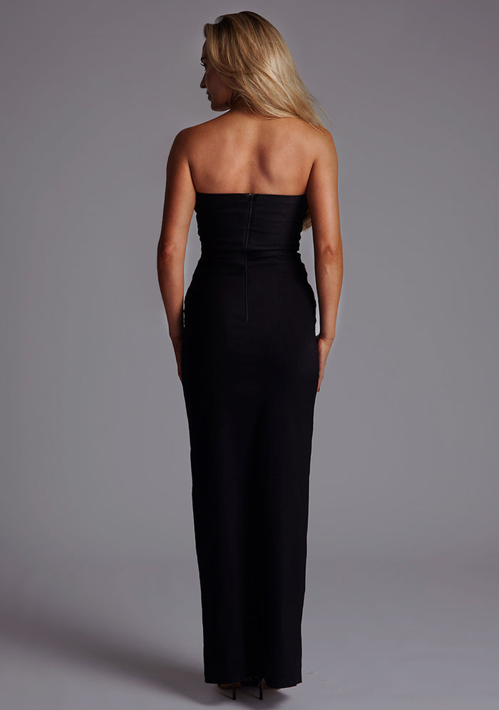 Back image of a model wearing the Vesper Alaya Bandeau Maxi Dress in Black, featuring a clean strapless back, centre-back zip closure, and refined silhouette.
