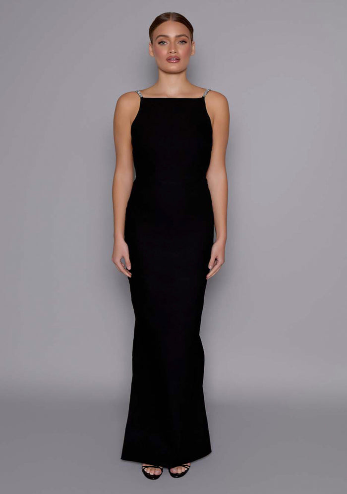 Front image of a model wearing the VSPR Alba Open Back Maxi Dress in Black with a structured square neckline and body skimming silhouette, standing against a grey studio backdrop.