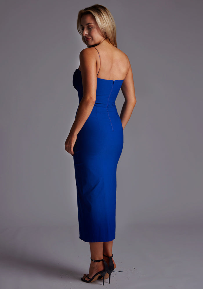 Back quarter image of a model wearing a cobalt midaxi dress with a charming sweetheart neckline with a ruched front design, delicate thin straps and graceful front skirt split. The design featured is the Vesper Alex Cobalt Midaxi Dress