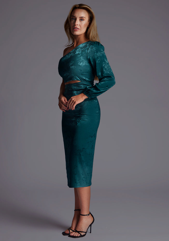 Side front image of a model in the Vesper Alice One Sleeve Midi Dress in Pine Green revealing the subtle side waist cut-out and slim midi-length silhouette.