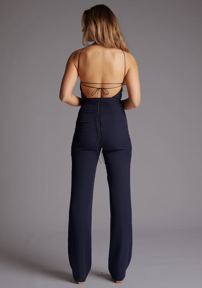 Back image of a model wearing the Vesper Amanda Halterneck Wide Leg Jumpsuit in Navy showcasing the halterneck strap design, clean back finish, and wide-leg trousers.