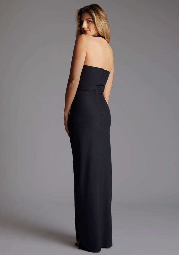 Side back image of a model wearing the Vesper Amira Halter Neck Maxi Dress in Black, capturing the sleek halter neckline and clean lines flowing into a floor-length skirt.