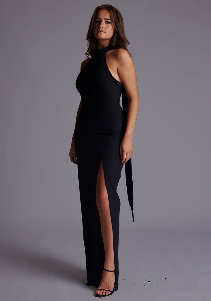 Side front image of a model wearing the Vesper Ariella High Neck Maxi Dress in Black showcasing the fluid body-skimming drape, refined tailoring, and subtle front skirt split for graceful movement.