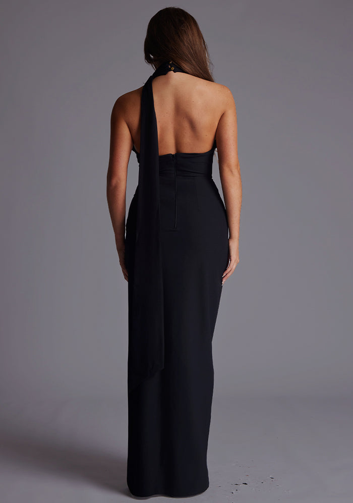 Back image of a model wearing the Vesper Ariella High Neck Maxi Dress in Black, featuring a striking open back, clean halter finish, and sweeping maxi length.