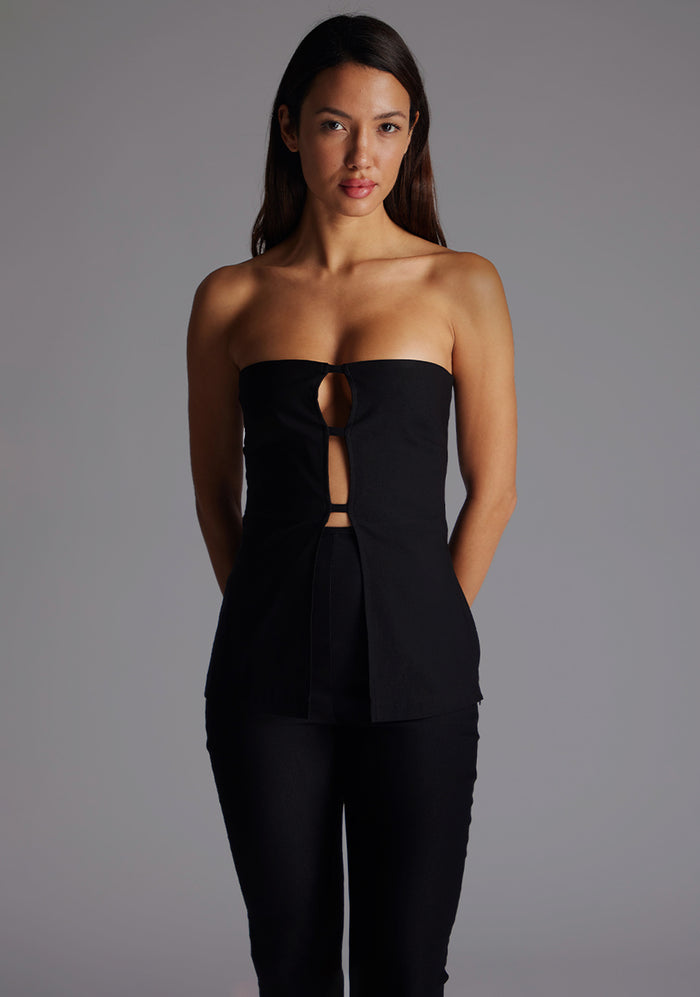 Close-up image highlighting the Vesper Augusta Bandeau Longline Top in Black, showcasing the smooth stretch fabric, clean strapless neckline, and subtle front cut-out detail, standing against a grey studio backdrop.