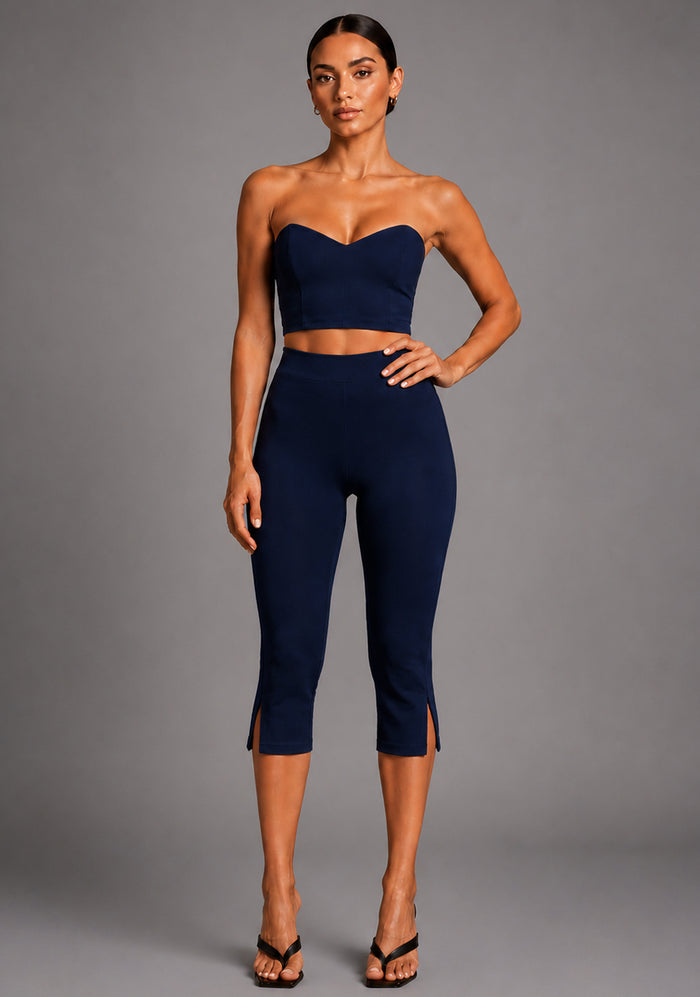 Front image of a model wearing the VSPR Benedetta Strapless Navy Crop Top with Capri Navy Trousers in navy, featuring a semi-V neckline, strapless fitted silhouette, and tailored high-waisted trousers, standing against a grey studio backdrop.