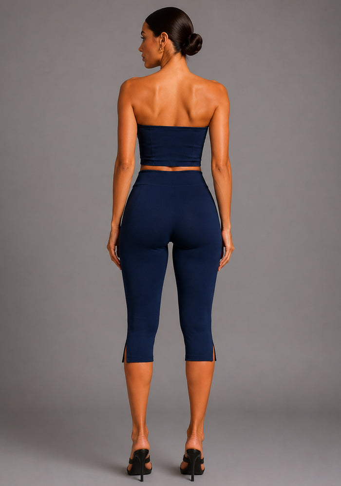 Back image of a model wearing the VSPR Benedetta Strapless Navy Crop Top with Capri Navy Trousers in navy, featuring a clean strapless back, figure-enhancing fit, and high-waisted tailored trousers against a grey studio backdrop.