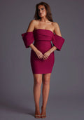 Front image of a model wearing the Vesper Beven Off-Shoulder Statement Mini Dress in Berry with an elegant off-shoulder neckline, billowy sleeves, and a sleek slim-fit silhouette, standing against a grey studio backdrop.