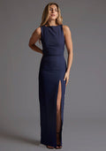 Front image of a model wearing the Vesper Brodi Backless High Neck Maxi Dress in Navy with a sleek sleeveless cut and elegant front skirt split, standing against a grey studio backdrop