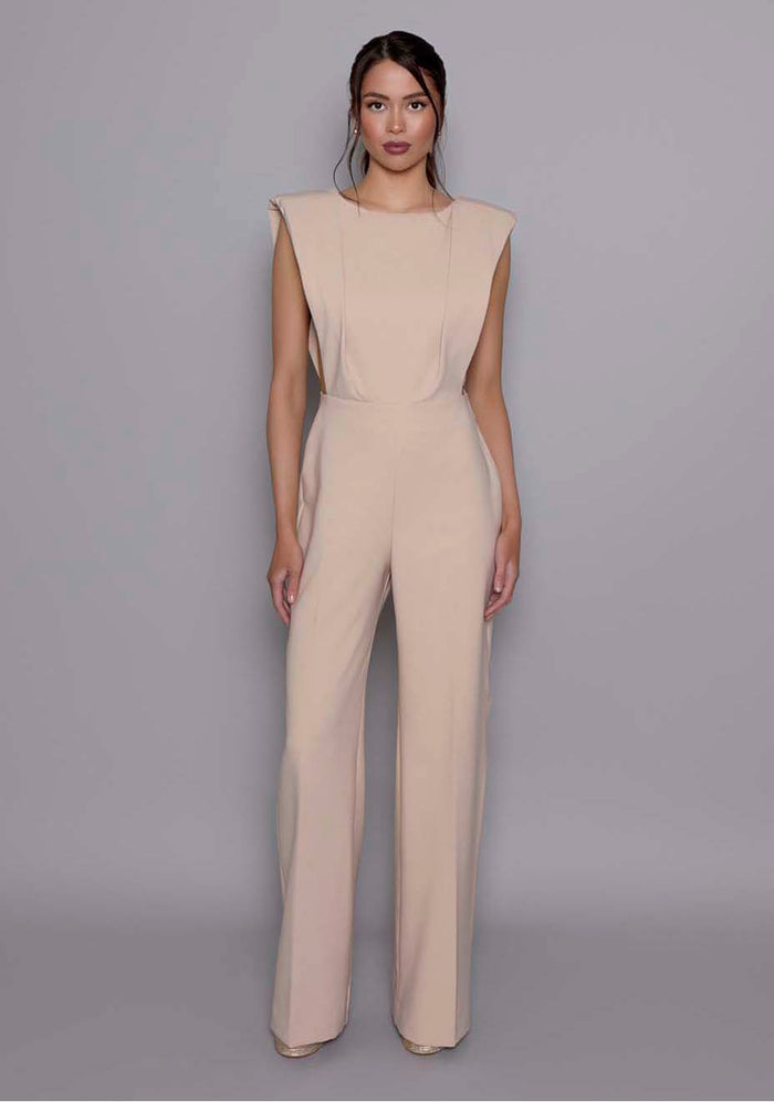 Model wearing the VSPR Bronte Stone open-back Jumpsuit featuring structured shoulders, a sculpted bodice, and wide-leg trousers, standing against a gray studio backdrop.