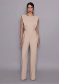 Model wearing the VSPR Bronte Stone open-back Jumpsuit featuring structured shoulders, a sculpted bodice, and wide-leg trousers, standing against a gray studio backdrop.