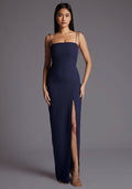 Front image of a model wearing the Vesper Bronte Tie Strap Maxi Dress in Navy with a straight neckline, slim-fit silhouette, and elegant front skirt split, posed against a grey studio backdrop.