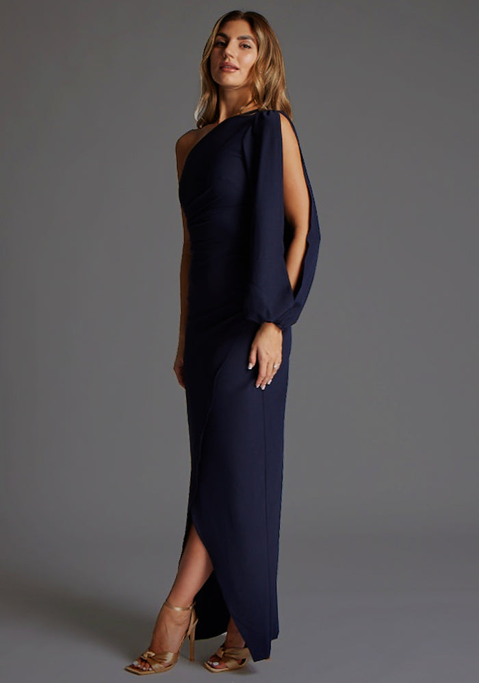 Side front image of a model wearing the Vesper Brooklyn One Shoulder Drape Sleeve Maxi Dress in Navy, showcasing the wrap-around detail and fluid draped sleeve.