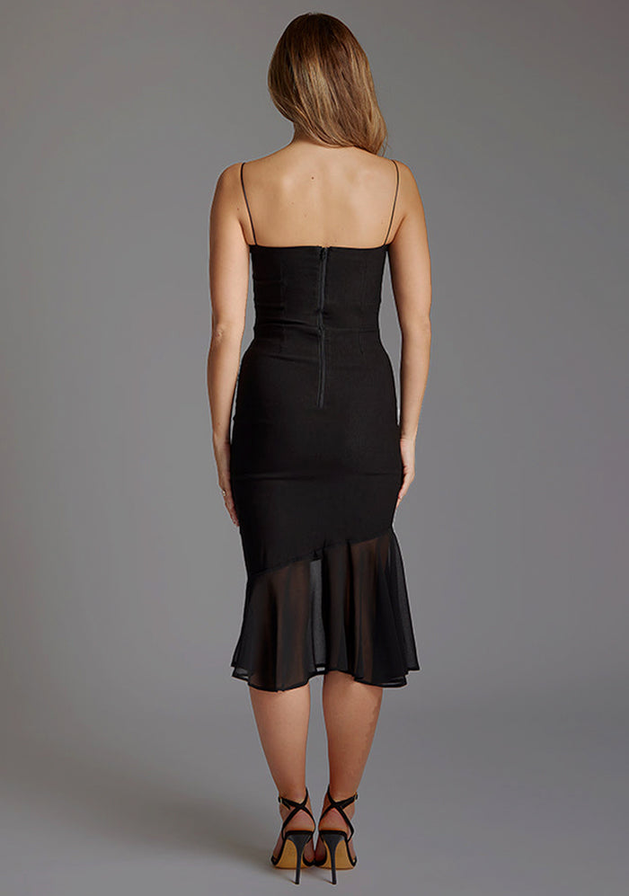 Back image of a model wearing a black frill hem midi dress with a straight neckline with thin straps and a contrast fabric frill hem. The design featured is the Vesper Buffy Frill Hem Square Neckline Midi Dress in Black.