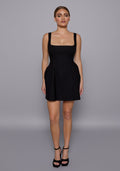 Model wearing the VSPR Camille Black Mini Dress with a square neckline and wide straps, styled with a soft A-line silhouette, standing against a minimalist grey backdrop.