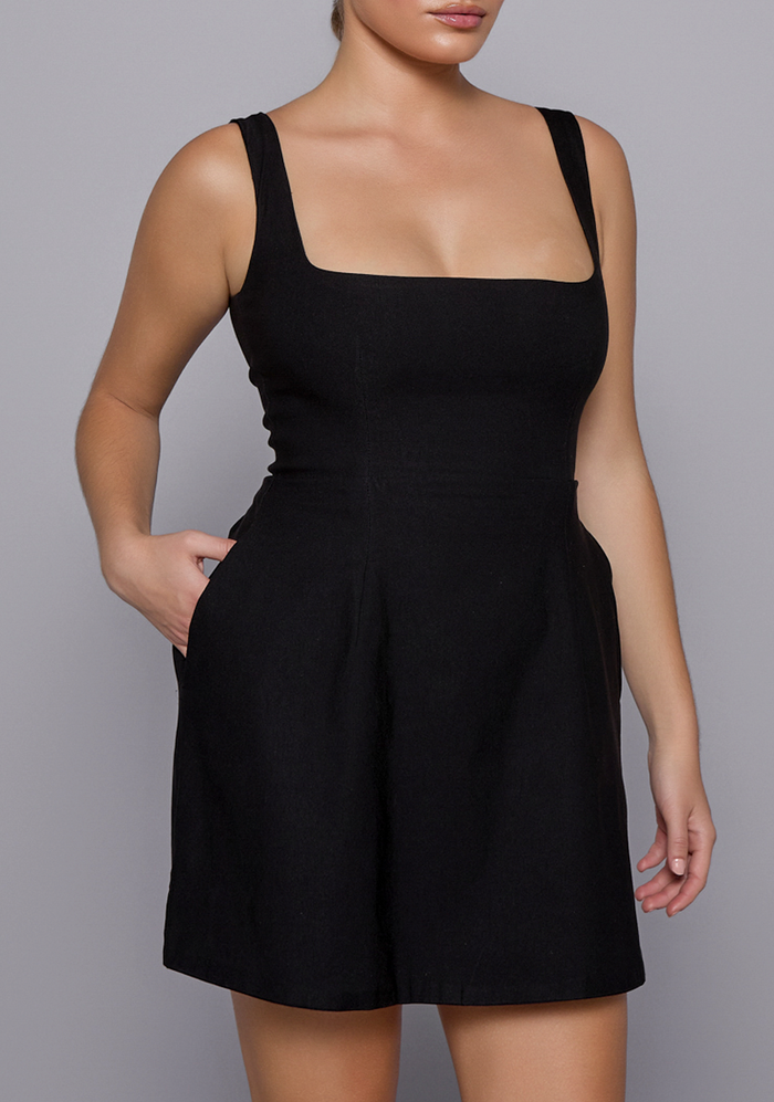 Close-up side-front view of the VSPR Camille Mini Dress in Black, capturing the sharp lines of the neckline and the curve-hugging bodice that flows into a subtle flare.