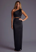 Front image of a blonde model wearing a black maxi dress with a alluring asymmetric one-shoulder design, subtle side cut-out and flattering wrap design skirt. The design featured is the Vesper Candace One-Shoulder Satin Maxi Dress in Black