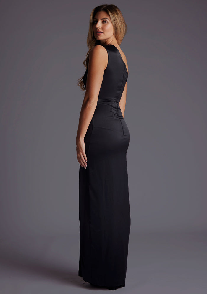 Side back image of a blonde model wearing a black maxi dress with an alluring asymmetric one-shoulder design, subtle side cut-out and flattering wrap design skirt. The design featured is the Vesper Candace One-Shoulder Satin Maxi Dress in Black