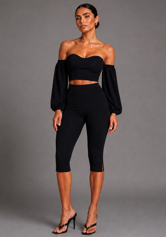 Front image of a model wearing the VSPR Belle Sweetheart Neckline Puff Sleeve Black Top featuring a sculpted sweetheart neckline, dramatic puff sleeves, and a figure-contouring fit. The design paired with Capri Black Cropped Trousers, pairstanding against a grey studio backdrop
