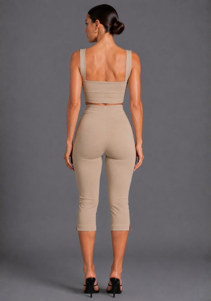 A woman shown from the back wearing a beige two-piece activewear set consisting of a cropped tank top and high-waisted capri leggings, paired with black heels, against a solid gray studio background.