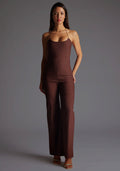 Front image of a model wearing the Vesper Cassidy Halterneck Wide Leg Jumpsuit in Chocolate, featuring a sleek halterneck design and wide-leg silhouette, standing against a grey studio backdrop.
