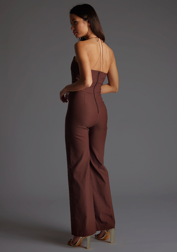 Side back image of a model wearing the Vesper Cassidy Halterneck Wide Leg Jumpsuit in Chocolate, showcasing the graceful halter tie detail at the back.