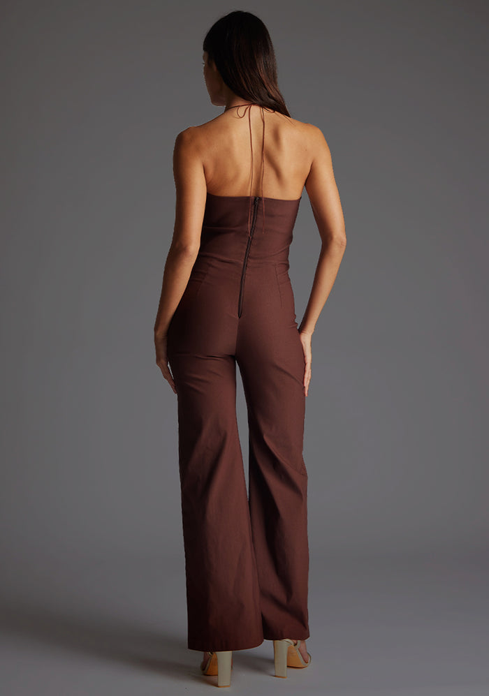 Back image of a model wearing the Vesper Cassidy Halterneck Wide Leg Jumpsuit in Chocolate, featuring the tied halter straps and discreet back zip.