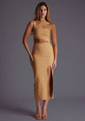 Front image of a blonde model wearing a coffee midaxi dress with a one shoulder design, tasteful cutout detailing, and a front skirt split. The design featured is the Vesper Cerellia Iced Coffee Midaxi Dress