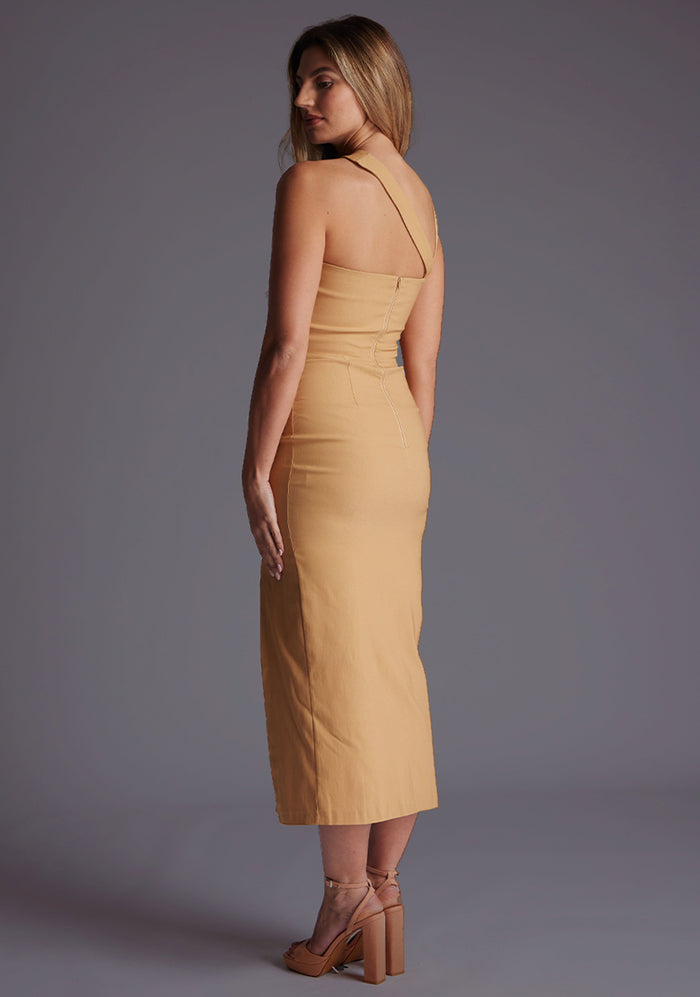 Back quarter image of a blonde model wearing a coffee midaxi dress with a one shoulder design, tasteful cutout detailing, and a front skirt split. The design featured is the Vesper Cerellia Iced Coffee Midaxi Dress
