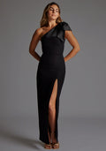 Front image of a model wearing the Vesper Ceylon One Shoulder Bow Maxi Dress in Black with an asymmetric bow neckline, sleek bodycon fit, front skirt split and maxi-length silhouette, standing against a neutral studio backdrop.