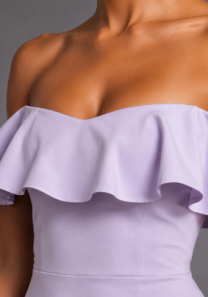 Close-up image of the VSPR Deirdre Bardot Off-Shoulder Frill Lilac Midaxi Dress showcasing the Bardot neckline, delicate frill detailing, and soft lilac fabric against a grey studio backdrop.