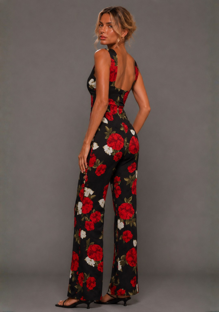 Side back image of a model wearing the VSPR Noelle V Neckline Black Floral Wide Leg Jumpsuit showcasing the low scoop back, flowing wide leg silhouette, and bold floral print against a grey studio backdrop.