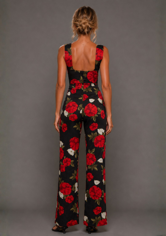 Back image of a model wearing the VSPR Noelle V Neckline Black Floral Wide Leg Jumpsuit featuring a low scoop back, tailored waist, and full-length wide leg silhouette against a grey studio backdrop.
